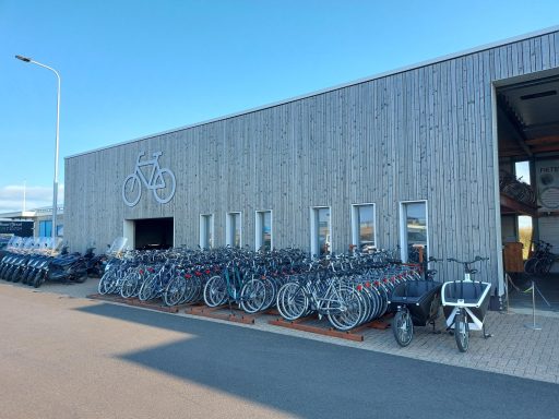 Fietsverhuur met een gebouw op de achtergrond en een rij fietsen ervoor.